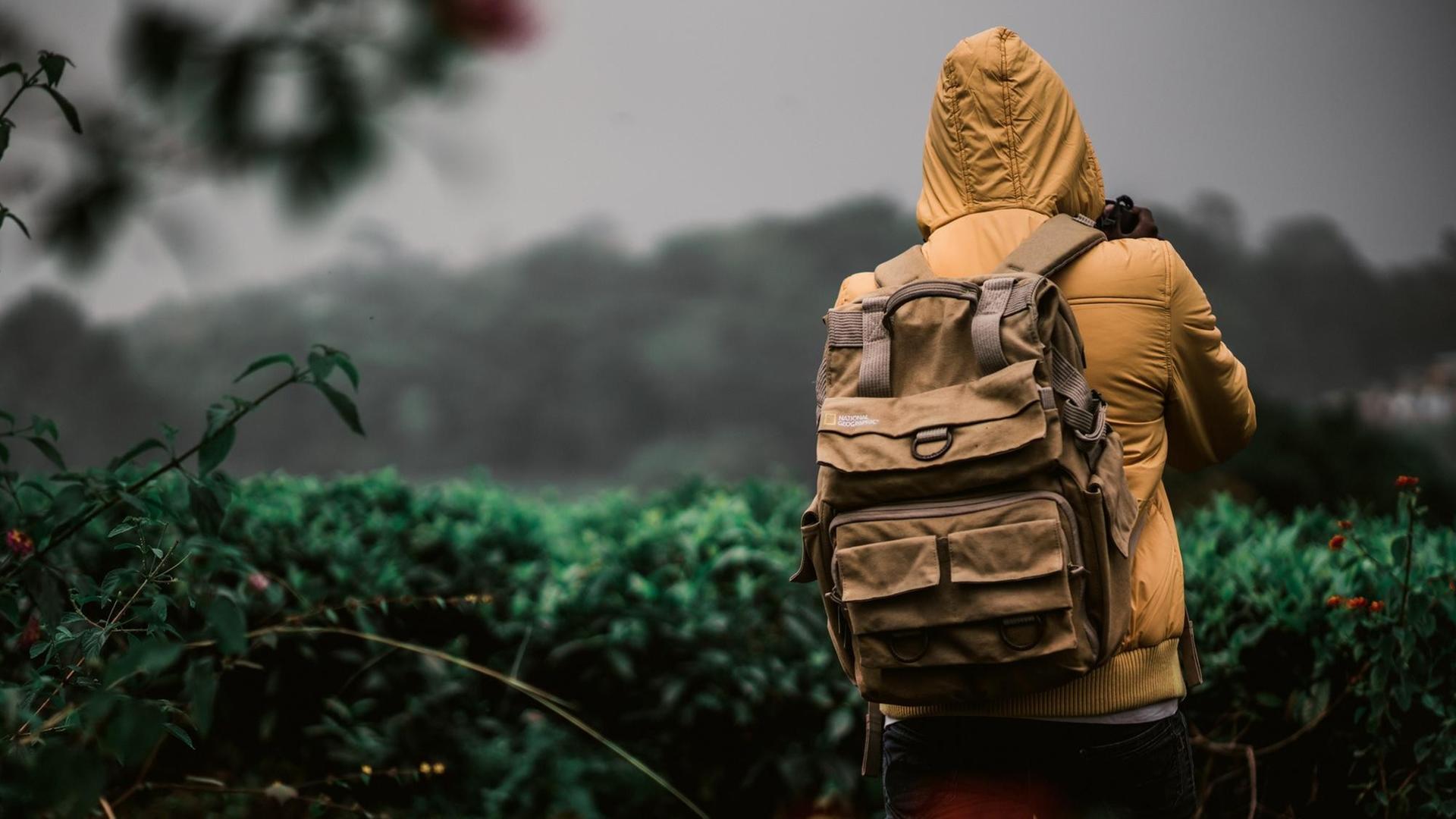 Ein Mann in einer gelben Jacke trägt einen Rucksack und steht in der Natur. Ein Mann in einer gelben Jacke trägt einen Rucksack und steht in der Natur.