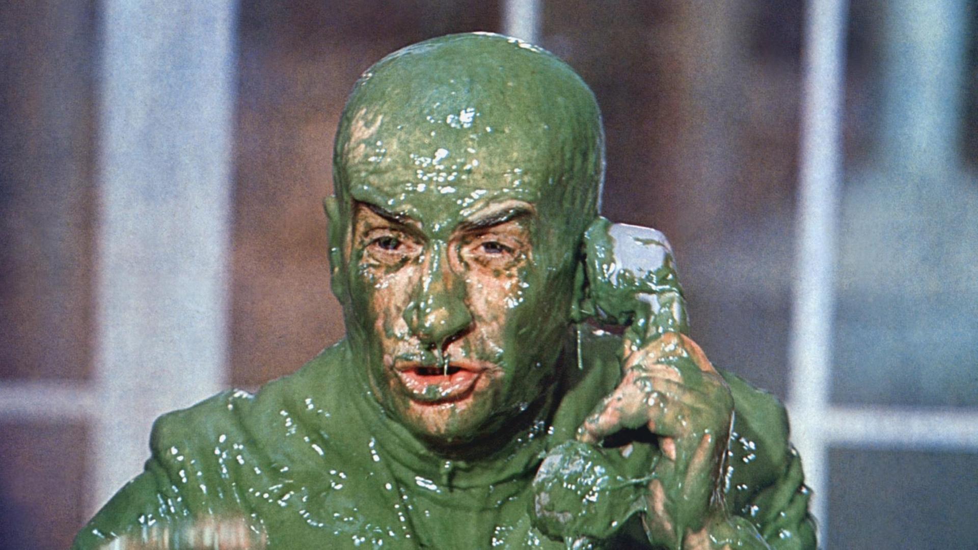 Der Schauspieler Louisde Funes versucht in einer Filmszene, ganz bedeckt von grünem Schleim, zu telefonieren.