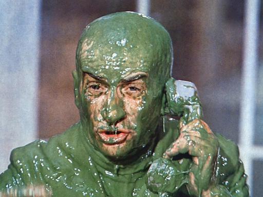 Der Schauspieler Louisde Funes versucht in einer Filmszene, ganz bedeckt von grünem Schleim, zu telefonieren.