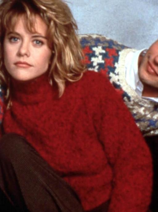Das Bild zeigt die Schauspieler Meg Ryan und Billy Crystal Händchen haltend. Meg Ryan trägt einen roten Pullover und Billy Crystal einen blauen mit rot-weißem Muster.