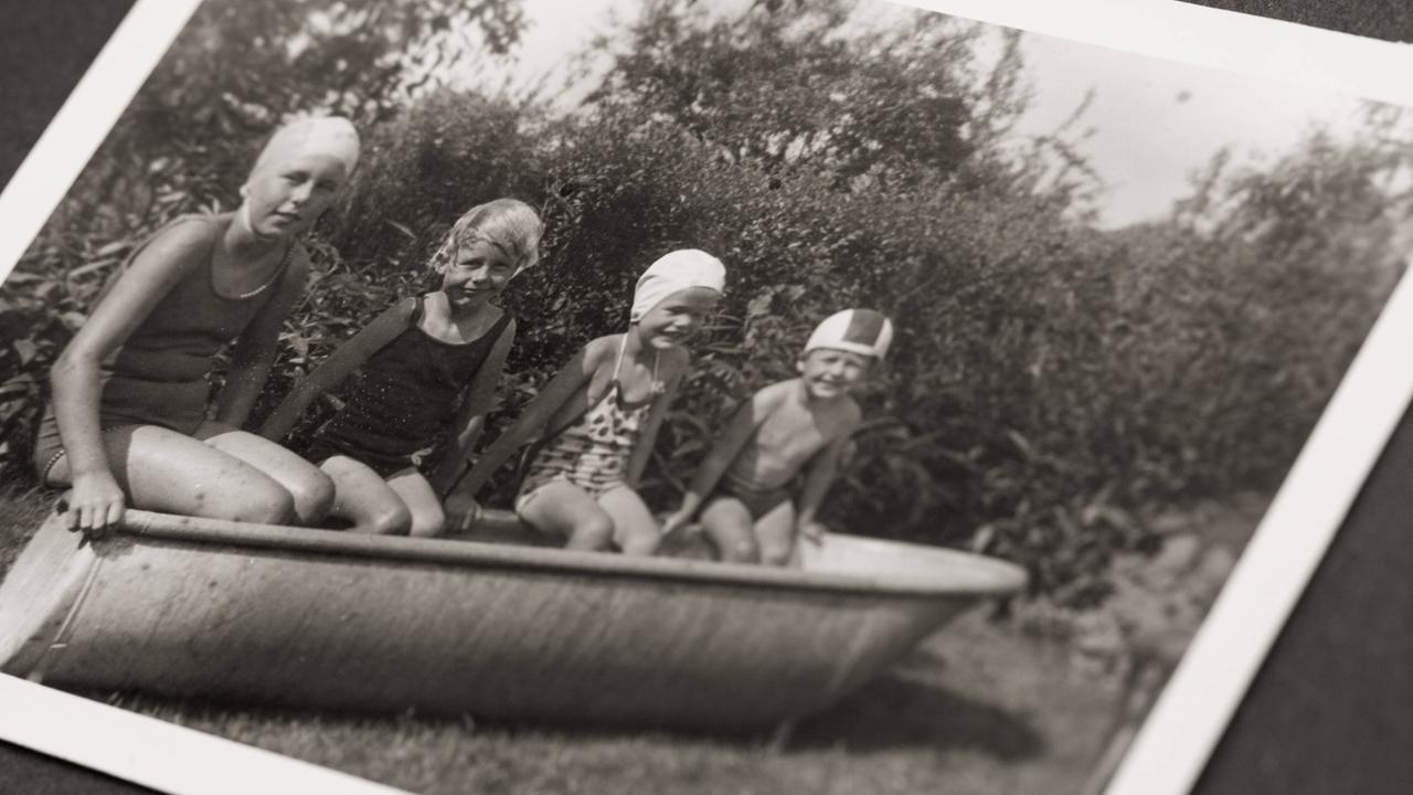 Kinder mit Badekappe sitzen in einer leeren Badewanne in einem Garten. Kinder mit Badekappe sitzen in einer leeren Badewanne in einem Garten.