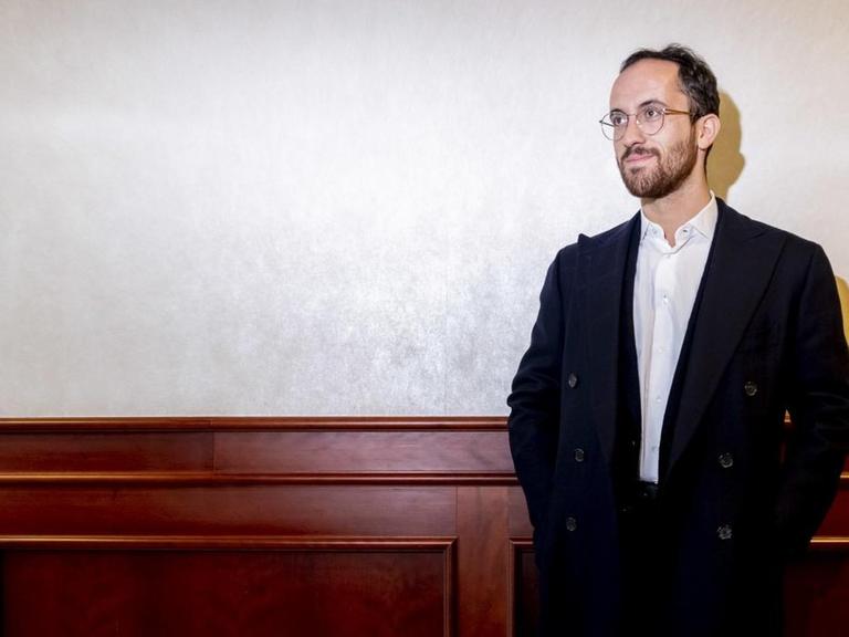 Der Pianist Igor Levit steht mit Händen in den Hosentaschen vor der holzgetäfelten Wand eines Flurs.