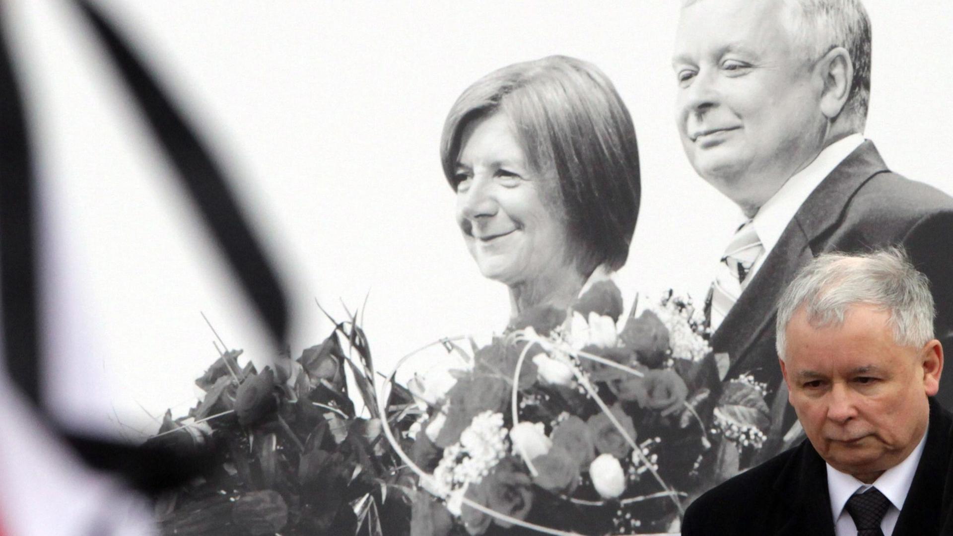Jaroslaw Kaczynski steht mit gesenktem Kopf vor einem Schwarz-Weiß-Bild seines Bruders Lech Kaczynski und seiner Frau, vorne links im Bild sind Teile der polnischen Flagge zu sehen. Jaroslaw Kaczynski steht mit gesenktem Kopf vor einem Schwarz-Weiß-Bild seines Bruders Lech Kaczynski und seiner Frau, vorne links im Bild sind Teile der polnischen Flagge zu sehen.