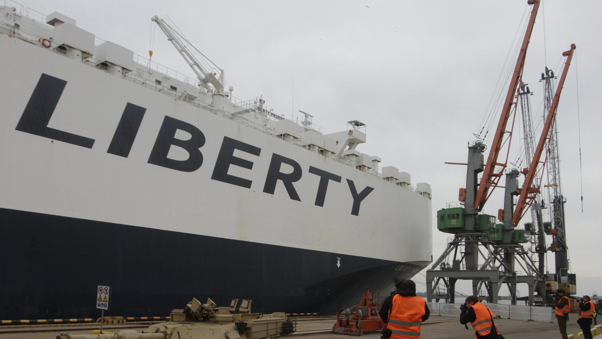 Rollender US-Panzer im Hafen von Riga, im Hintergrund ein Frachtschiff mit der Aufschrift "Liberty" und mehrere Kräne.