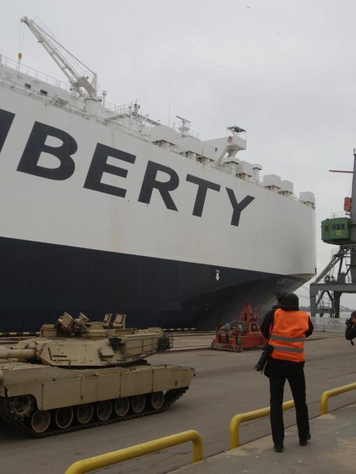Rollender US-Panzer im Hafen von Riga, im Hintergrund ein Frachtschiff mit der Aufschrift "Liberty" und mehrere Kräne.