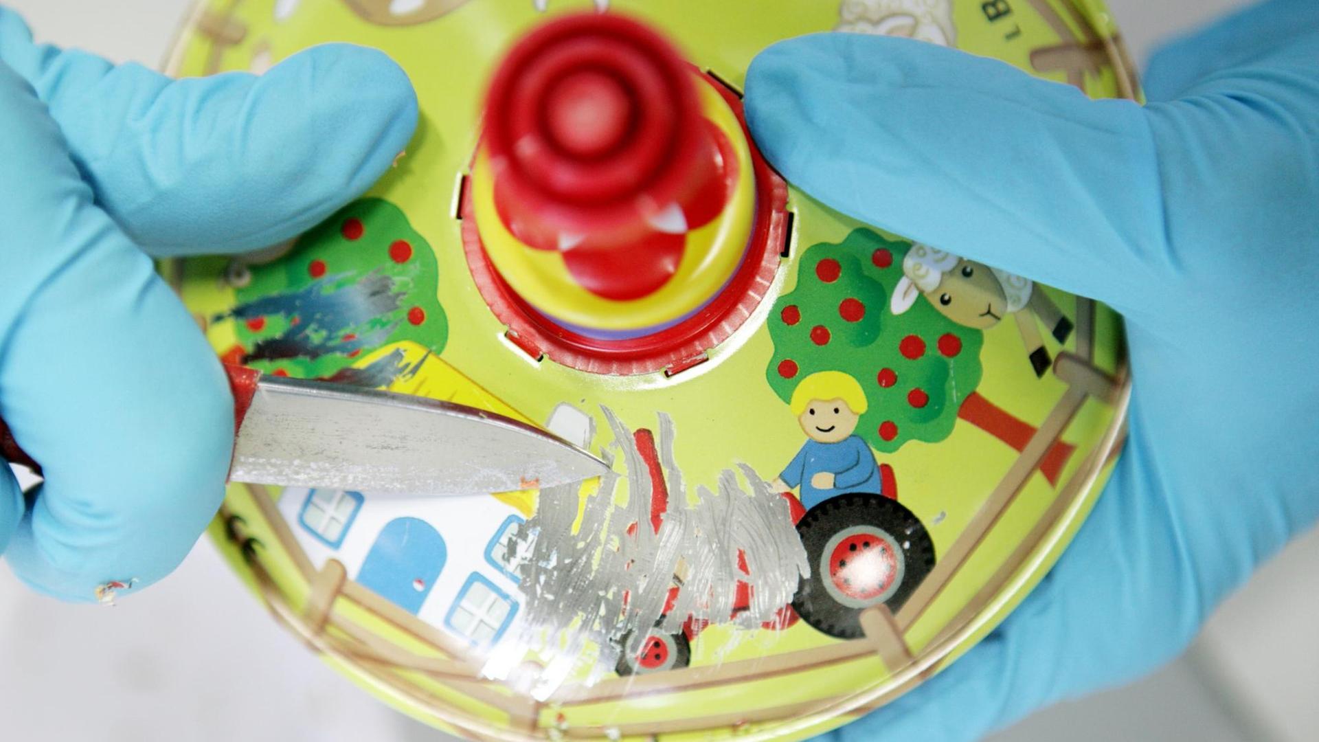 Von einem Spielzeugkreisel wird mit einem Messer bunter Lack abgeschabt. Von einem Spielzeugkreisel wird mit einem Messer bunter Lack abgeschabt.