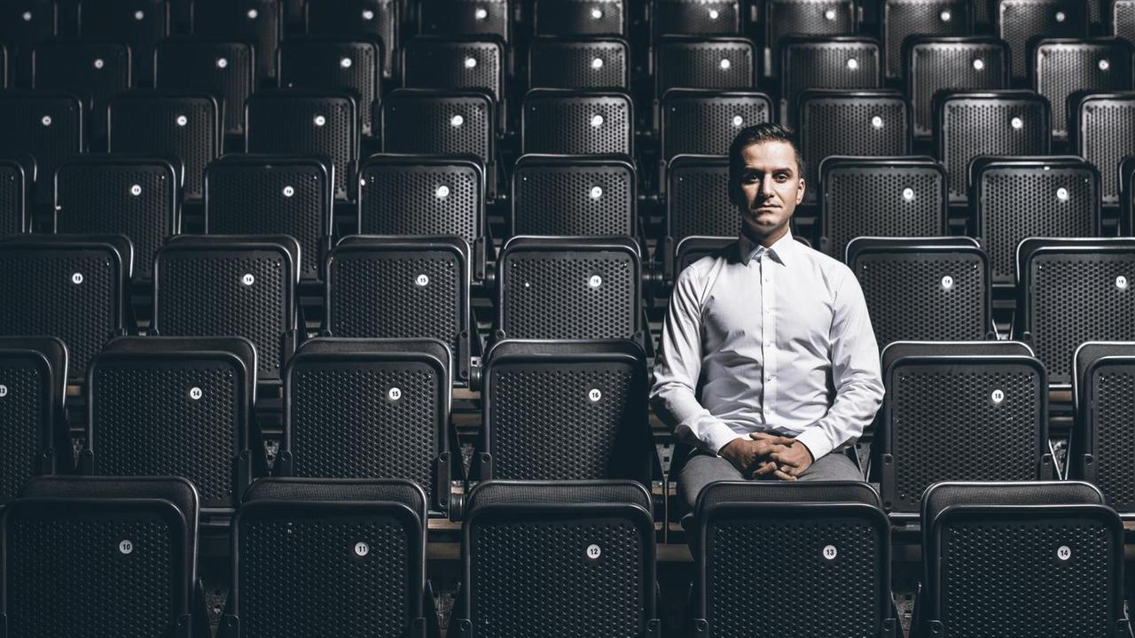 Der Stuttgarter Comedian Özcan Cosar sitzt alleine in einem Konzertsaal mit schwarzen Klappstühlen. Der Stuttgarter Comedian Özcan Cosar sitzt alleine in einem Konzertsaal mit schwarzen Klappstühlen.
