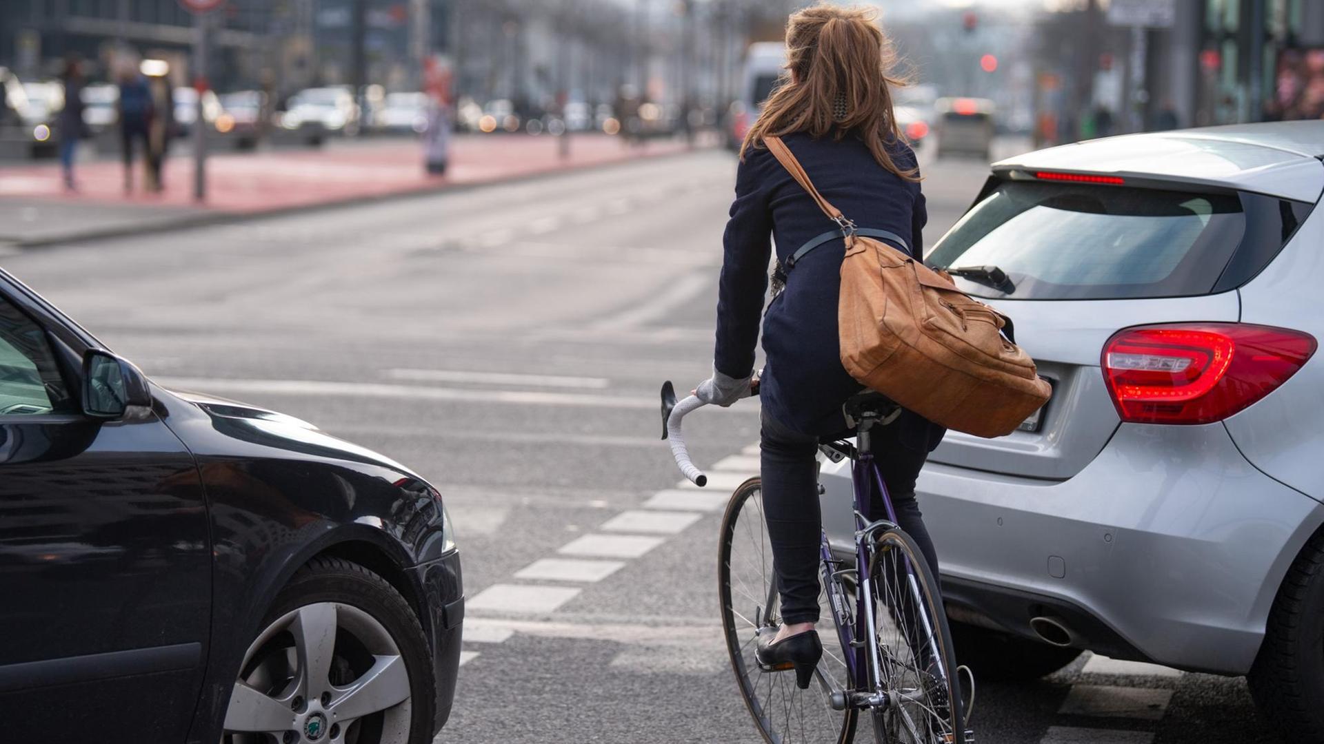 Berlin: Eine Fahrradfahrerin fährt auf einem Fahrradweg auf einer Kreuzung zwischen zwei Autos entlang. Berlin: Eine Fahrradfahrerin fährt auf einem Fahrradweg auf einer Kreuzung zwischen zwei Autos entlang.