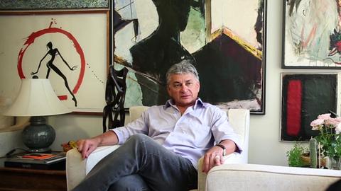 Chagas Freitas auf einem Sessel, vor Kunstwerken sitzend