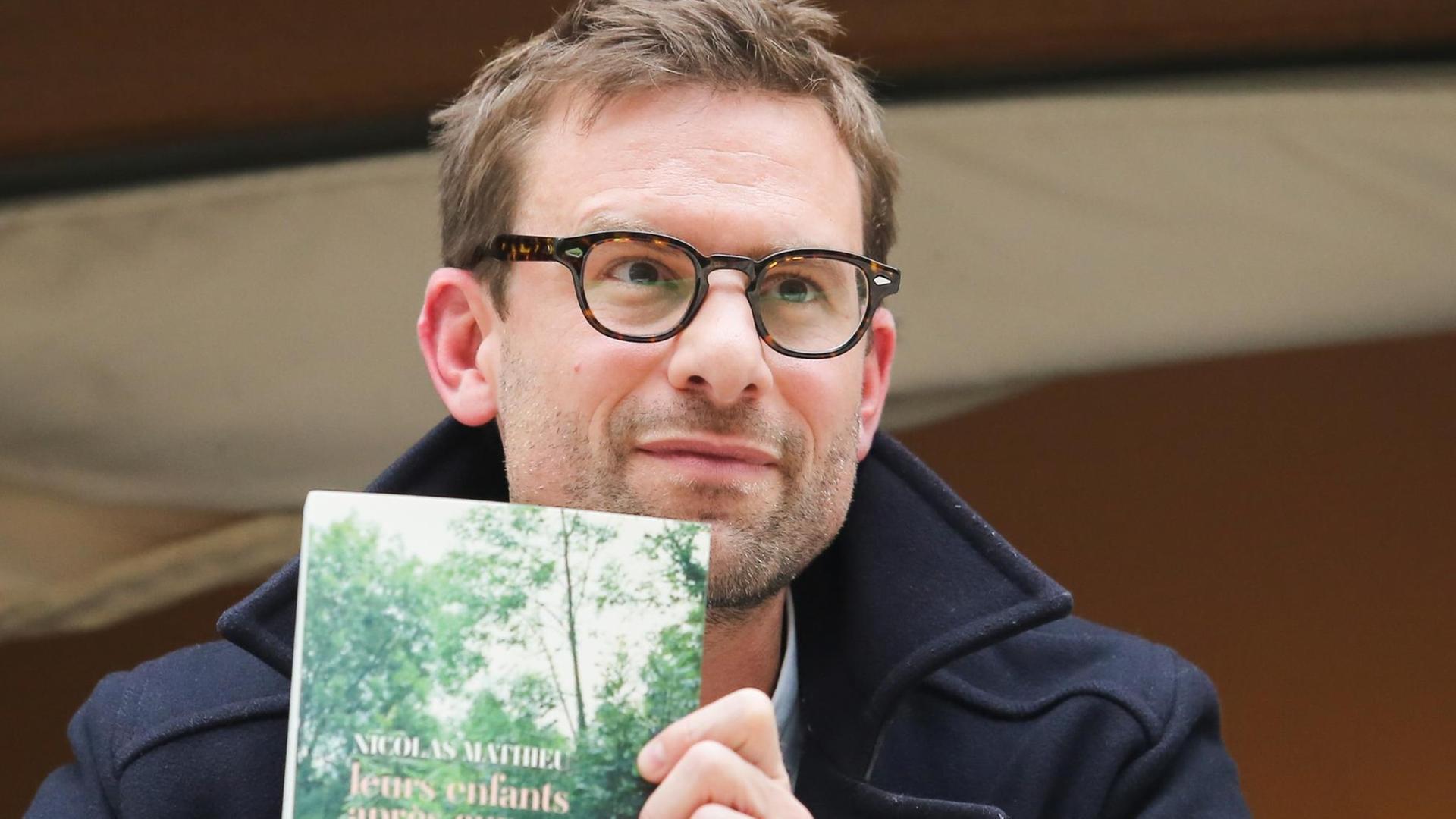 Der französische Autor Nicolas Mathieu mit seinem Buch "Les enfants après eux" nach der Auszeichnung mit dem Prix Goncourt, Frankreichs wichtigstem Literaturpreis. | dpa / picture alliance | Nasser Berzane/ABACAPRESS.COM | Der französische Autor Nicolas Mathieu mit seinem Buch "Les enfants après eux" nach der Auszeichnung mit dem Prix Goncourt, Frankreichs wichtigstem Literaturpreis. | dpa / picture alliance | Nasser Berzane/ABACAPRESS.COM |