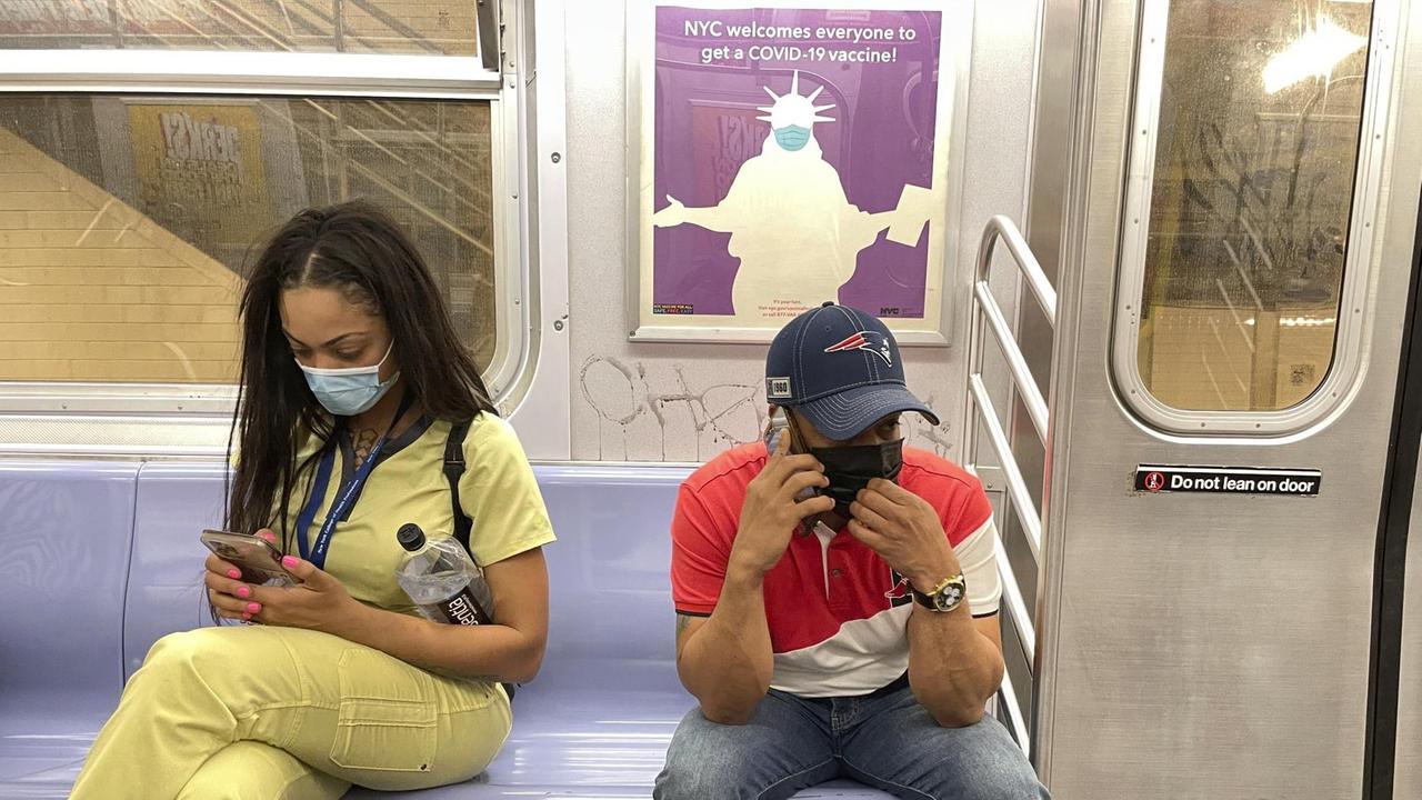 Fahrgäste in der New Yorker U-Bahn mit Mundschutz. Im Hintergrund ein Plakat mit der Freiheitsstatue, die Maske trägt. Fahrgäste in der New Yorker U-Bahn mit Mundschutz. Im Hintergrund ein Plakat mit der Freiheitsstatue, die Maske trägt.
