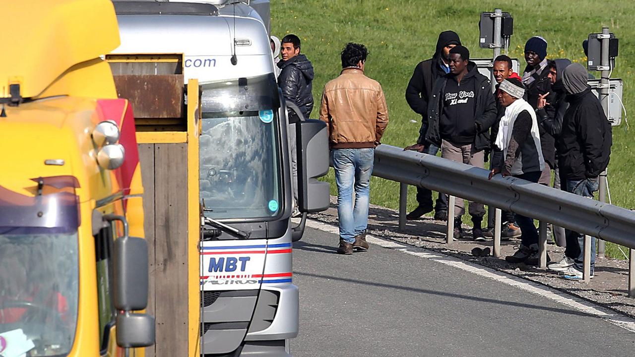 Flüchtlinge stehen an einer Straße, auf der mehrere Lkw fahren. Flüchtlinge stehen an einer Straße, auf der mehrere Lkw fahren.