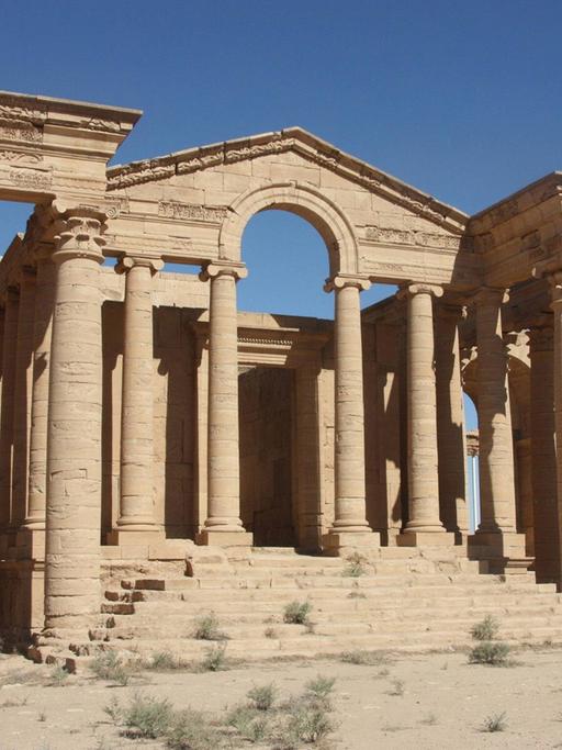Ein antiker Tempel mit zwei Seitenflügeln und einer Treppe ohne Dach steht in der Wüste.