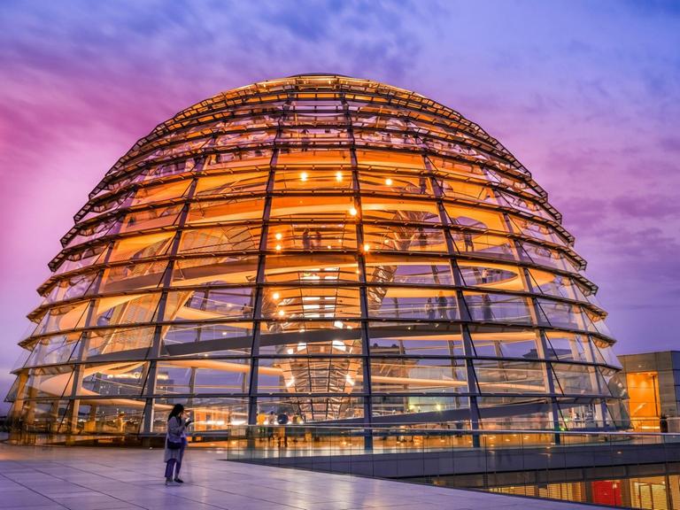 Die orange illuminierte Reichstagskuppel bei Abenddämmerung.