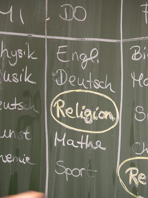 Eine Schülerin steht an einer Tafel, auf der ein Stundenplan mit Religionsunterricht geschrieben ist. Das Fach ist umkreist.