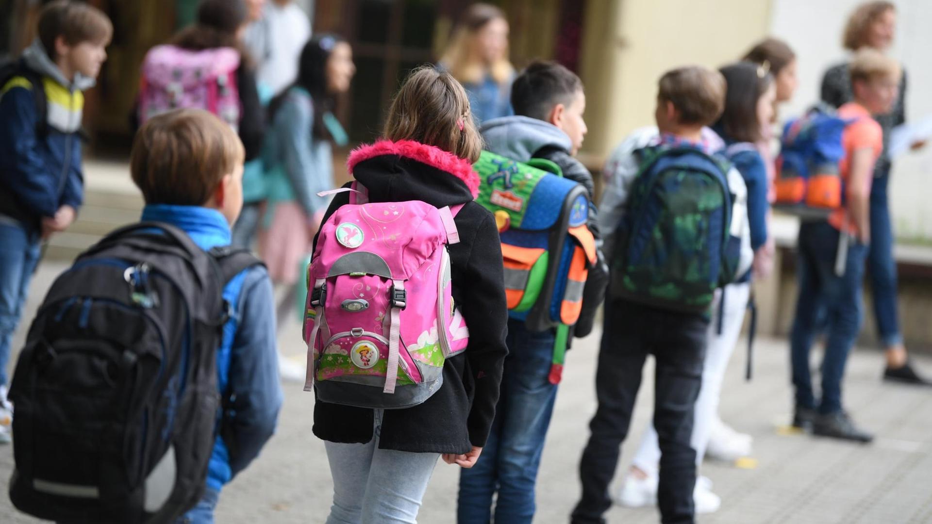 Schülerinnen und Schüler einer Grundschule stehen mit Abstand zueinander auf dem Schulhof Schülerinnen und Schüler einer Grundschule stehen mit Abstand zueinander auf dem Schulhof