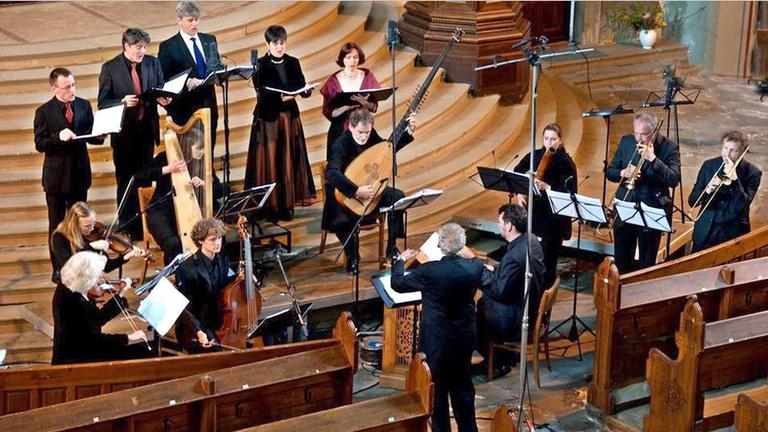 Ein Dirigent steht vor einer Gruppe von Sängern und Musikern, die alte Instrumente spielen Ein Dirigent steht vor einer Gruppe von Sängern und Musikern, die alte Instrumente spielen