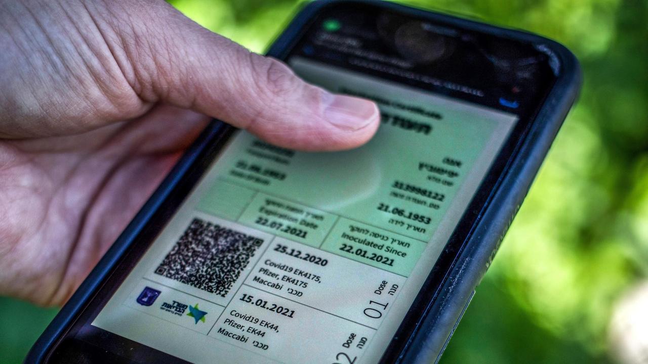 Ein Mann hält ein Smartphone in der Hand, auf dem der sogenannte "Grüne Pass" abgebildet ist. Ein Mann hält ein Smartphone in der Hand, auf dem der sogenannte "Grüne Pass" abgebildet ist.