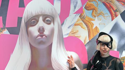 Die Musikerin Lady Gaga posiert in einem schwarzen Lederkostüm neben einem Bildnis von ihr, das der Künstler Jeff Koons angefertigt hat.