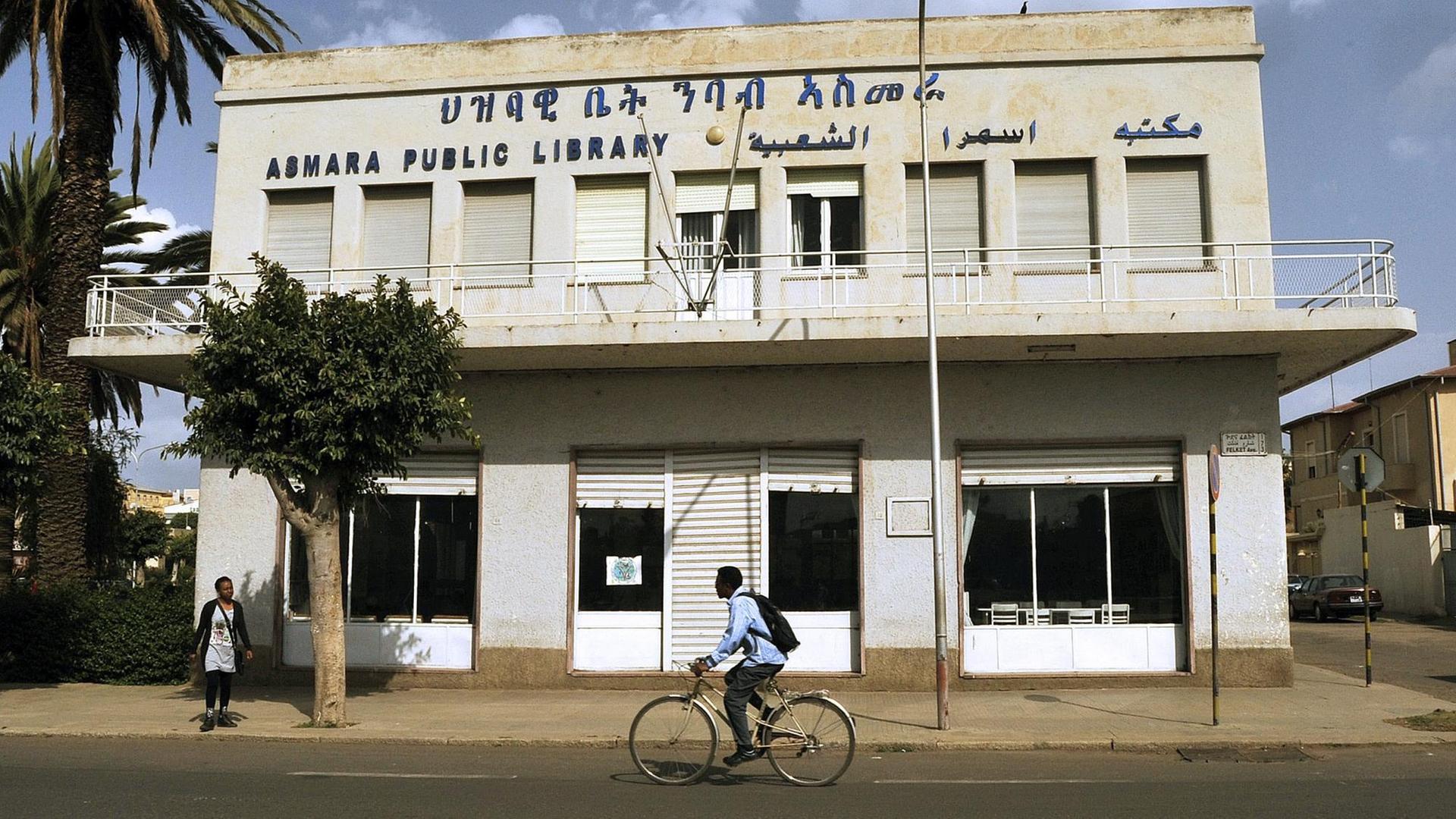 Ein Mann fährt mit einem Rad an der öffentlichen Bibliothek von Asmara, Eritreas Hauptstadt, entlang. Die Infrastruktur der Stadt ist sehr veraltet. Ein Mann fährt mit einem Rad an der öffentlichen Bibliothek von Asmara, Eritreas Hauptstadt, entlang. Die Infrastruktur der Stadt ist sehr veraltet.