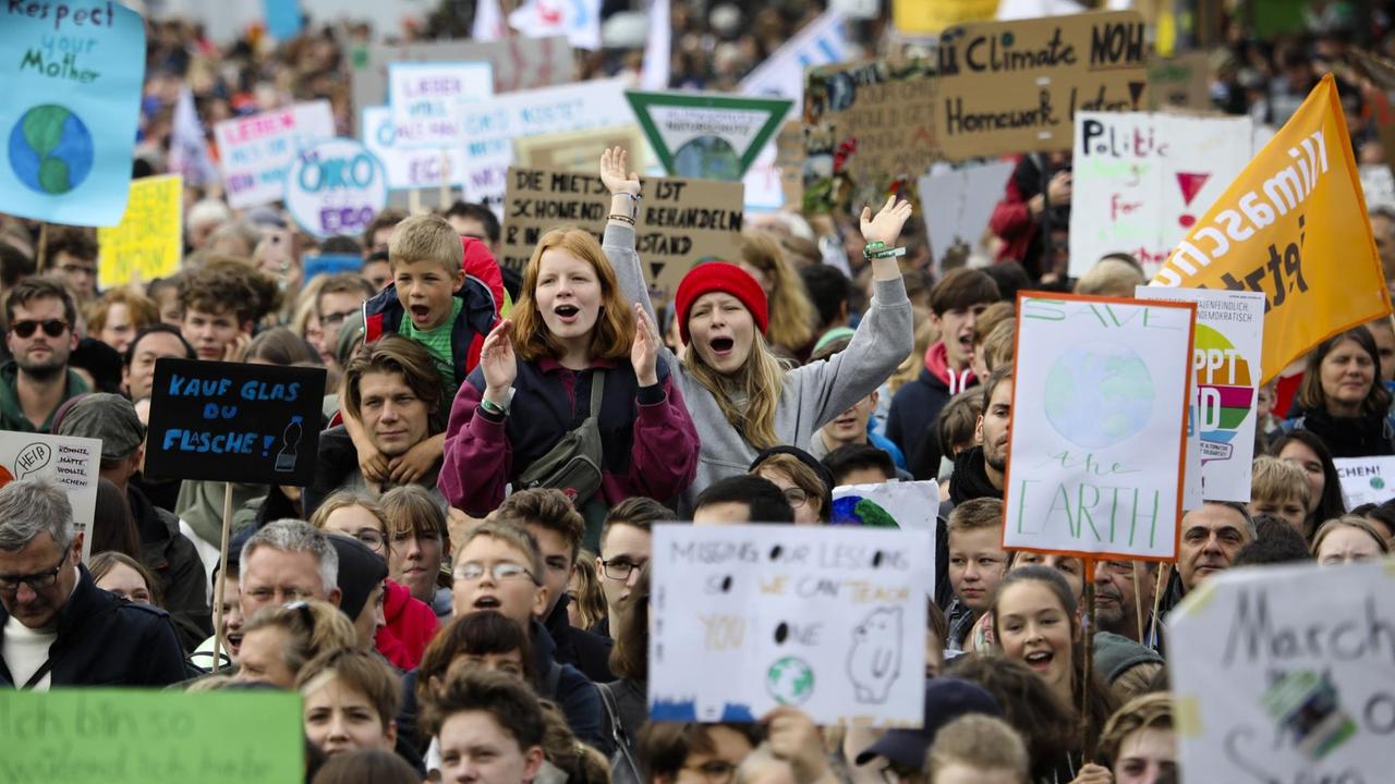 Eine große Gruppe von Menschen. Einzelne halten Schilder in die Höhe, auf denen Botschaften für Klimaschutz stehen.