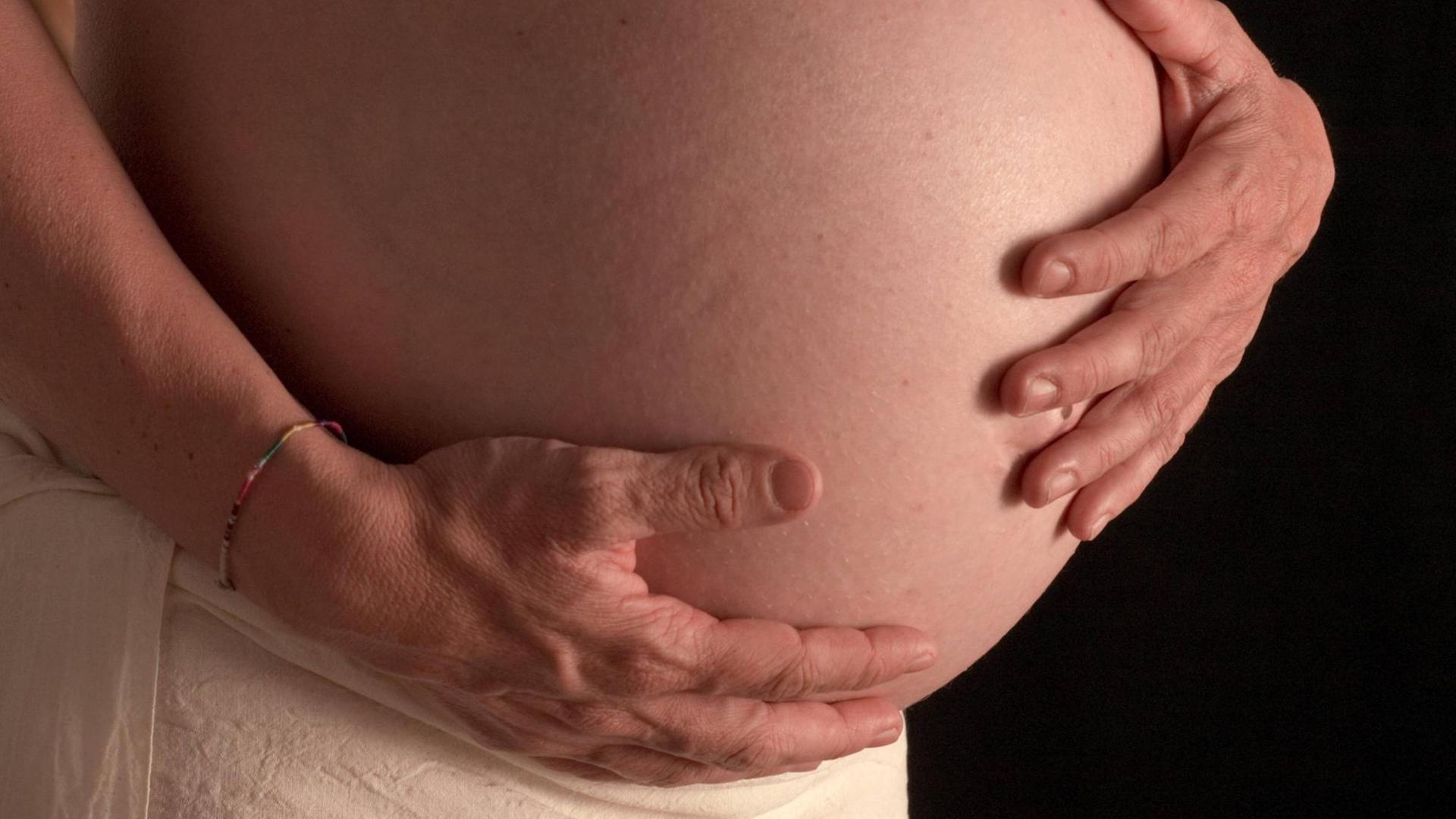 Eine schwangere Frau legt die Hände auf ihren Bauch. Eine schwangere Frau legt die Hände auf ihren Bauch.