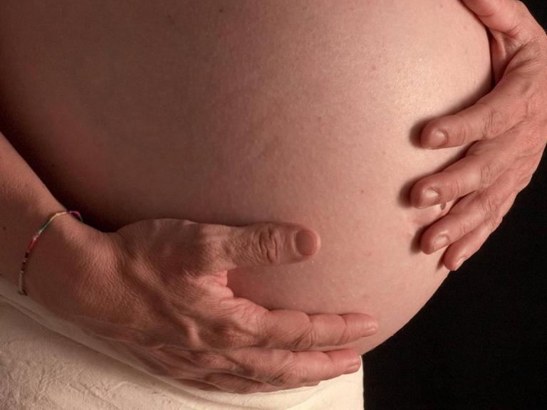 Eine schwangere Frau legt die Hände auf ihren Bauch.