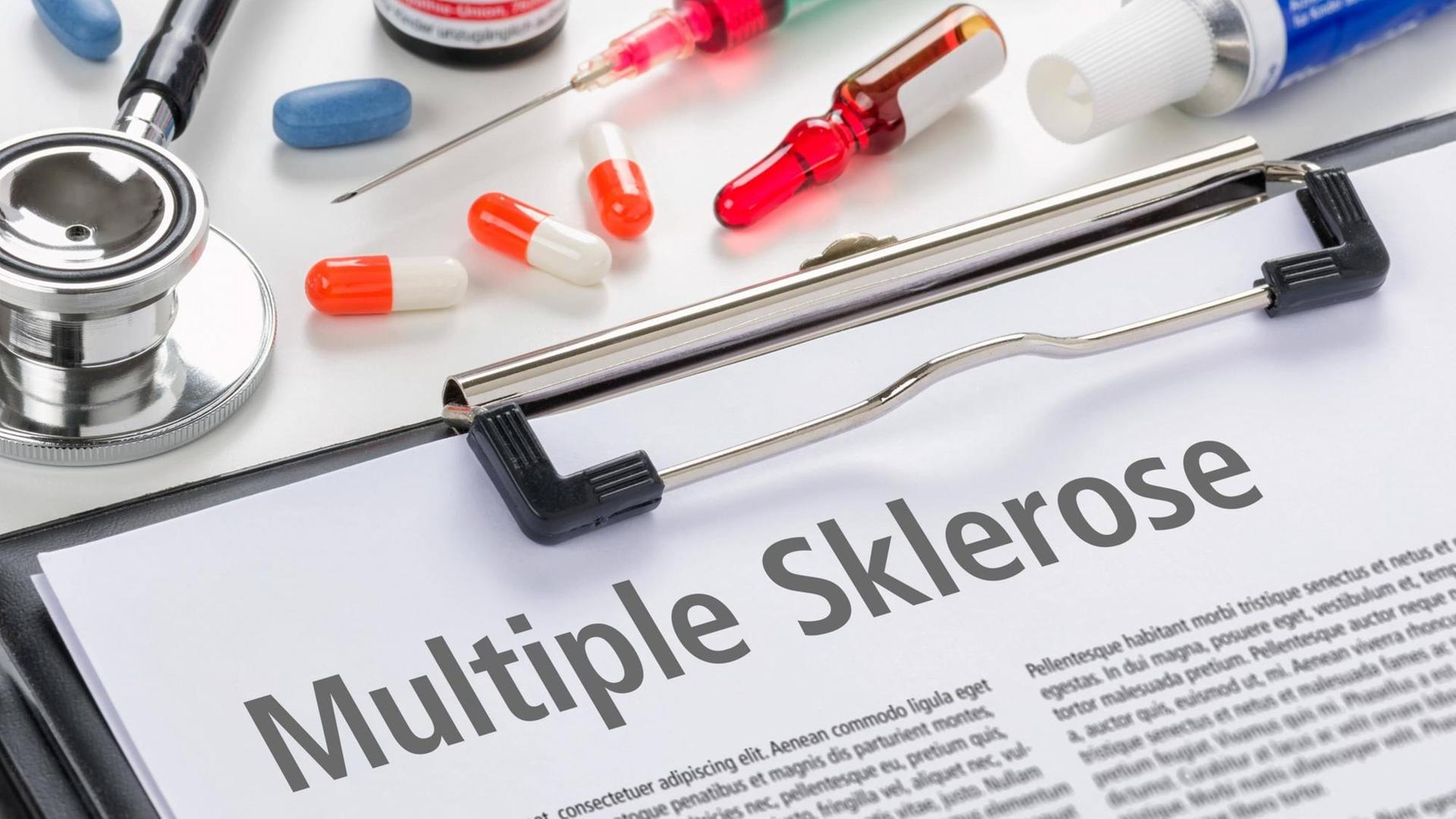 Ein Dokument mit der Aufschrift Multiple Sklerose, im Hintergrund Pillen, Spritzen und anderes medizinisches Zubehör