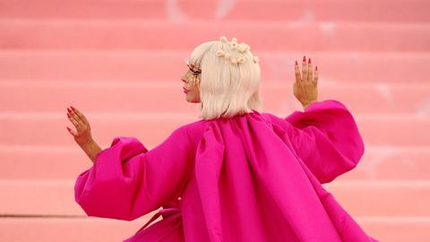 Profil der Musikerin Lady Gaga mit seitlich erhobenen Händen, in einer wallenden pinken Robe