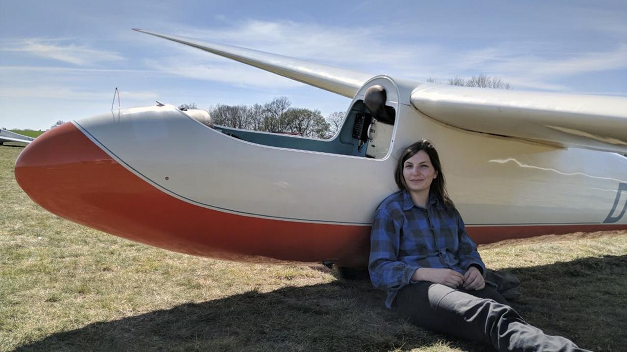 Die Autorin und Segelfliegerin Lea Eichhorn sitzt mit ausgestreckten Beinen auf dem Boden, angelegt an ein Segelflugzeug.