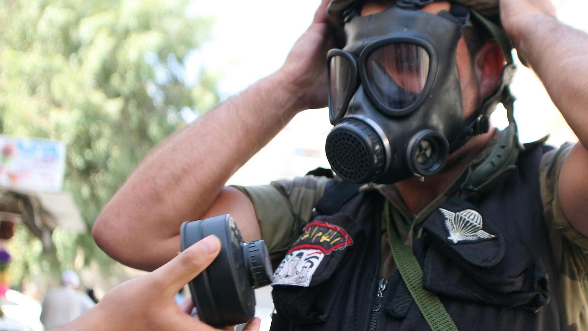 Ein syrischer Soldat hat eine Gasmaske auf, eine Hand reicht ihm einen neuen Filter.