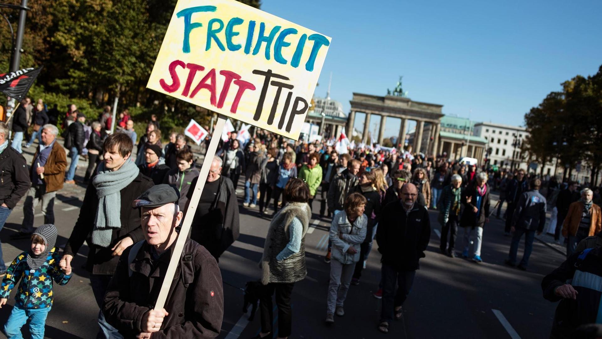 Ein Mann trägt ein Schild mit der Aufschrift: "Freiheit statt TTIP". Mit vielen anderen Demonstranten läuft er auf der Straße, im Hintergrund ist das Brandenburger Tor.