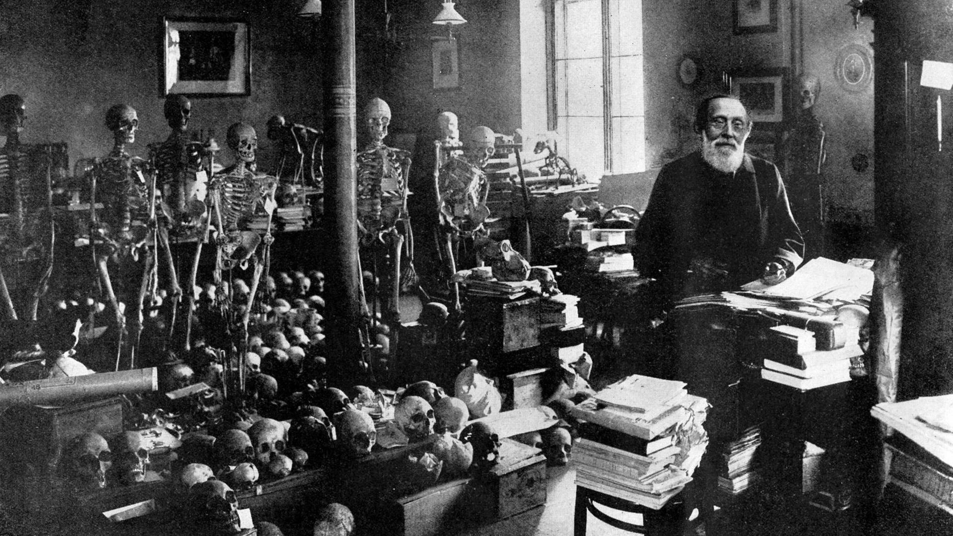 Ein Schwarz-Weiß Foto zeigt den Mediziner Rudolf Virchow neben zahlreichen Skeletten und Schädeln im Berliner Institut für Pathologie Berlin