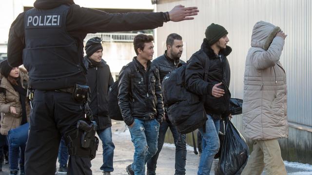 Ein Polizist streckt den Arm aus und weist Flüchtlingen den Weg