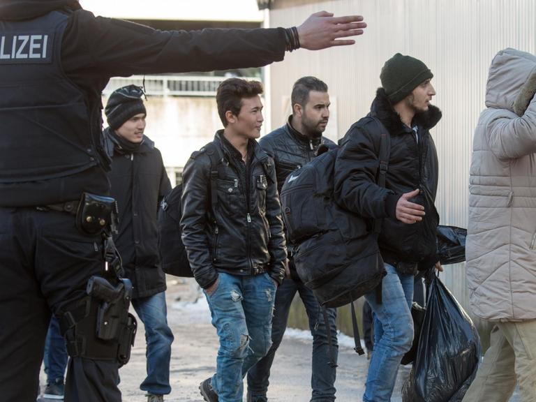 Ein Polizist streckt den Arm aus und weist Flüchtlingen den Weg