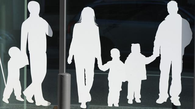 Man sieht weiße Figuren von einem Vater mit Kind und einer Familie mit Kindern, die auf einer Glasscheibe kleben