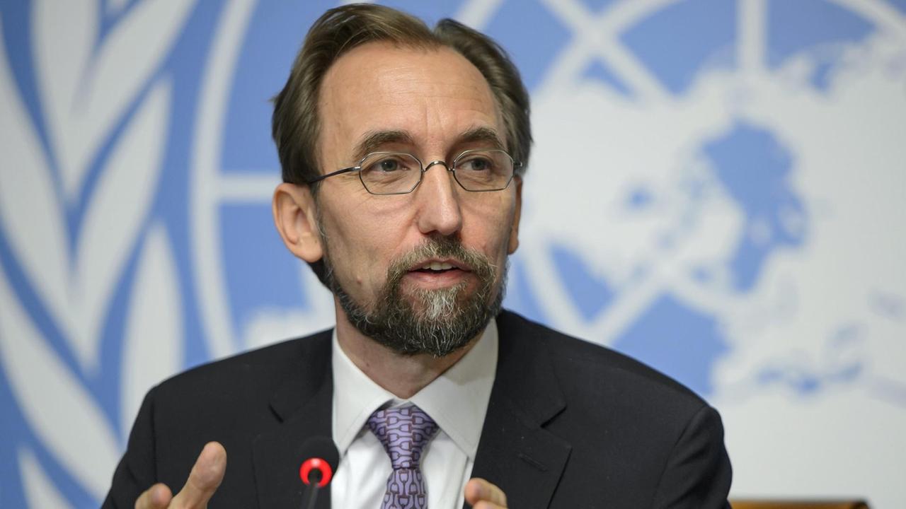 Hussein spricht und gestikuliert vor einem Mikrofon. Im Hintergrund ein hellblau-weißer Backdrop mit dem Logo der UNO.