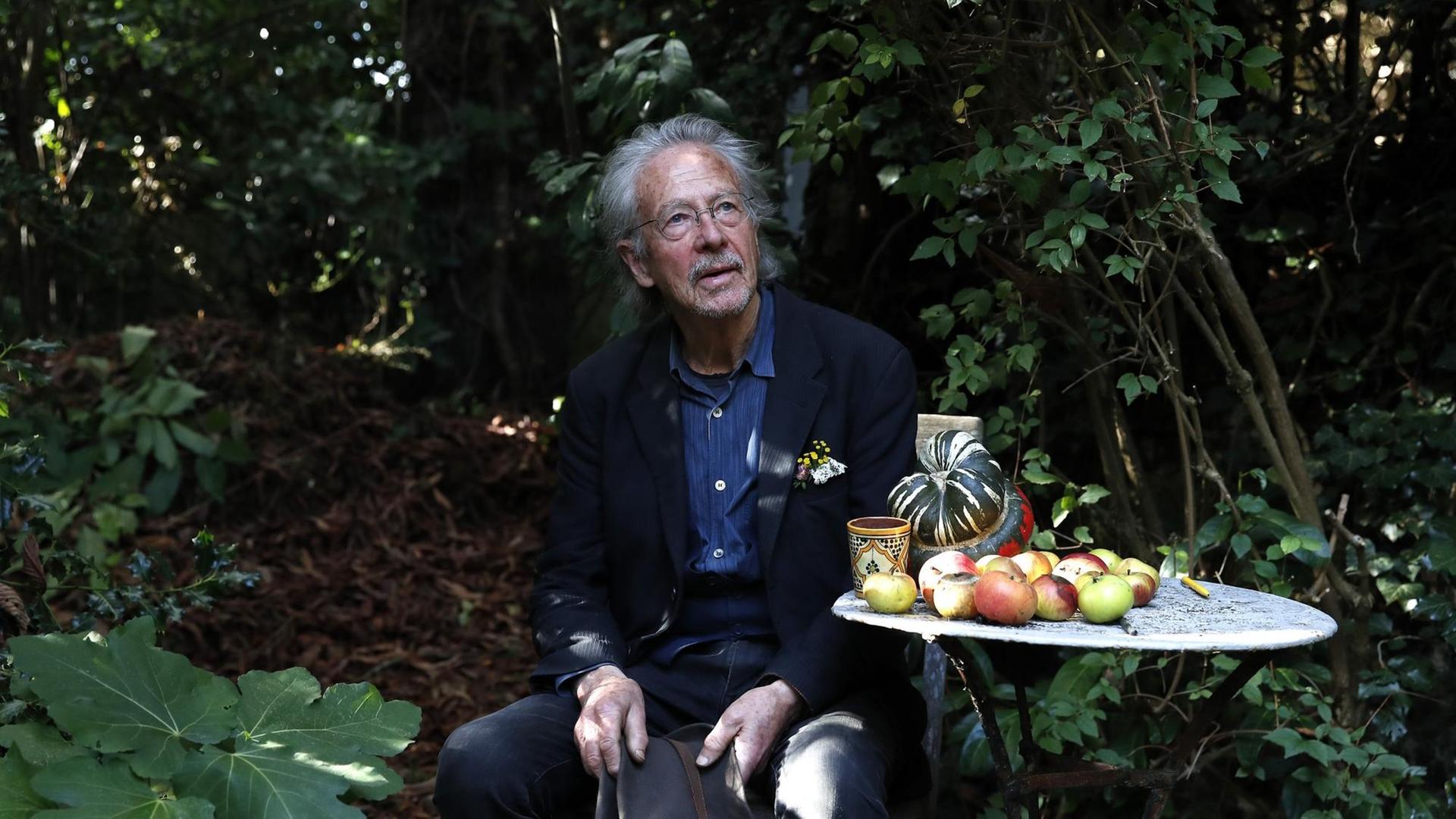 Der Schriftsteller Peter Handke sitzt an einem kleinen runden Tisch mit Äpfeln in seinem Garten in Chaville in der Nähe von Paris.