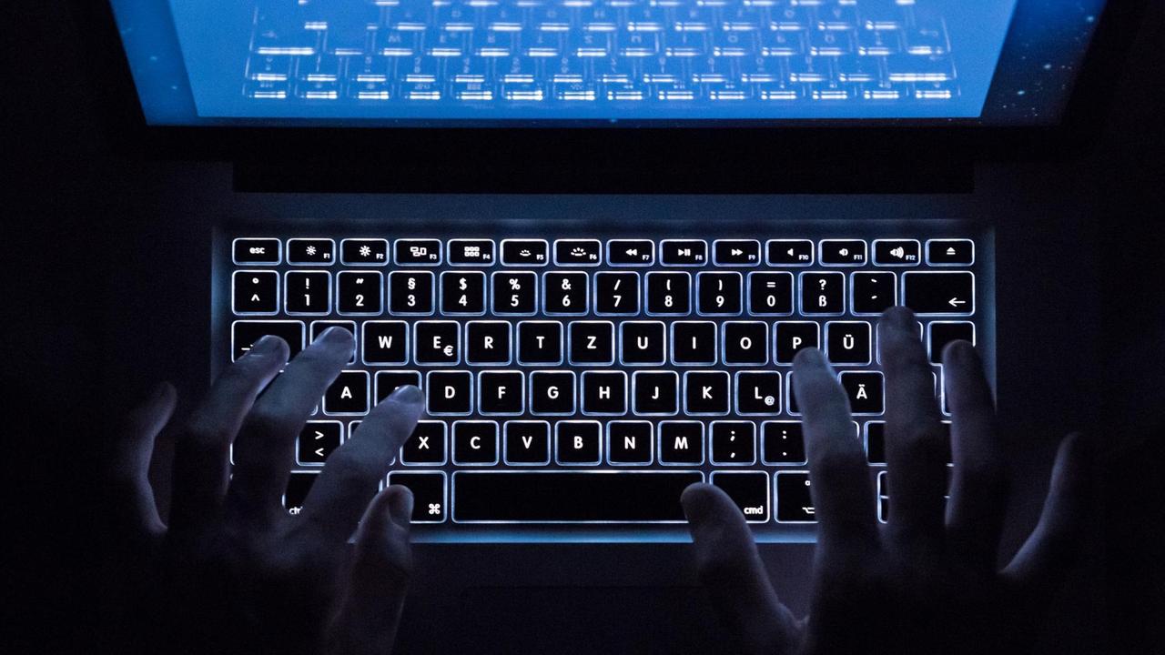 Zwei Hände auf einer beleuchteten Tastatur im Dunklen