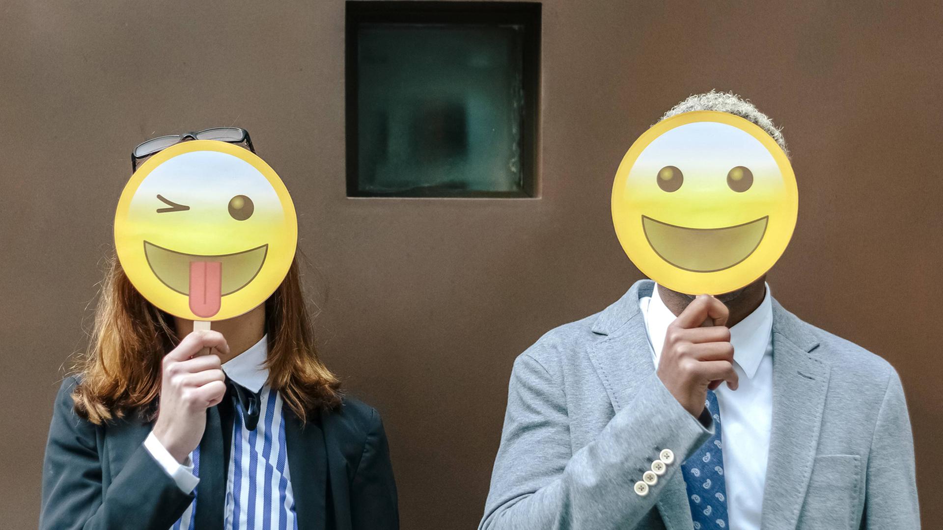 Eine Frau und ein Mann verdecken ihre Gesicher mit Emoji-Masken Eine Frau und ein Mann verdecken ihre Gesicher mit Emoji-Masken