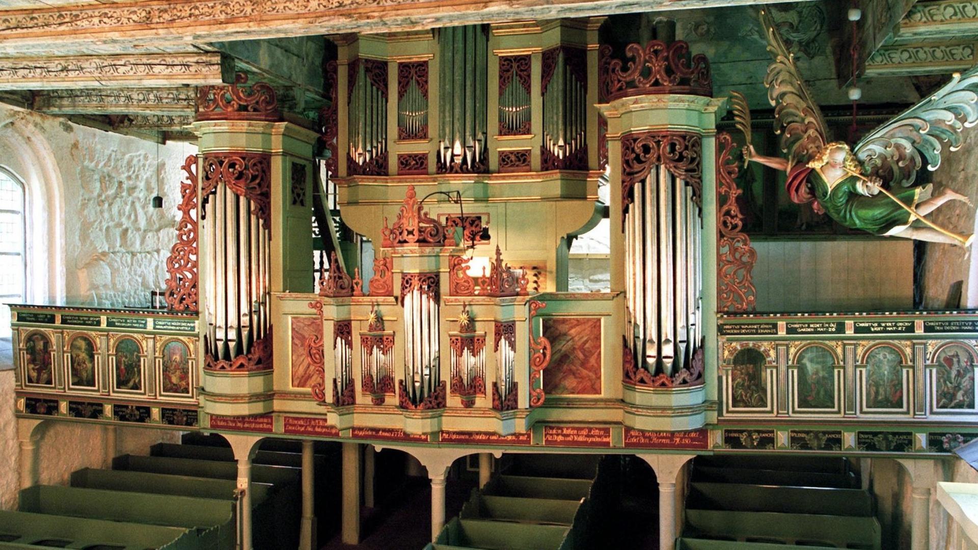 Das historische Instrument ist von grün-, rot-, goldfarbenem Holz umgeben, links und rechts befindet sich jeweils eine Empore, auf deren Aussenseiten gibt es Heiligenabbildungen Das historische Instrument ist von grün-, rot-, goldfarbenem Holz umgeben, links und rechts befindet sich jeweils eine Empore, auf deren Aussenseiten gibt es Heiligenabbildungen