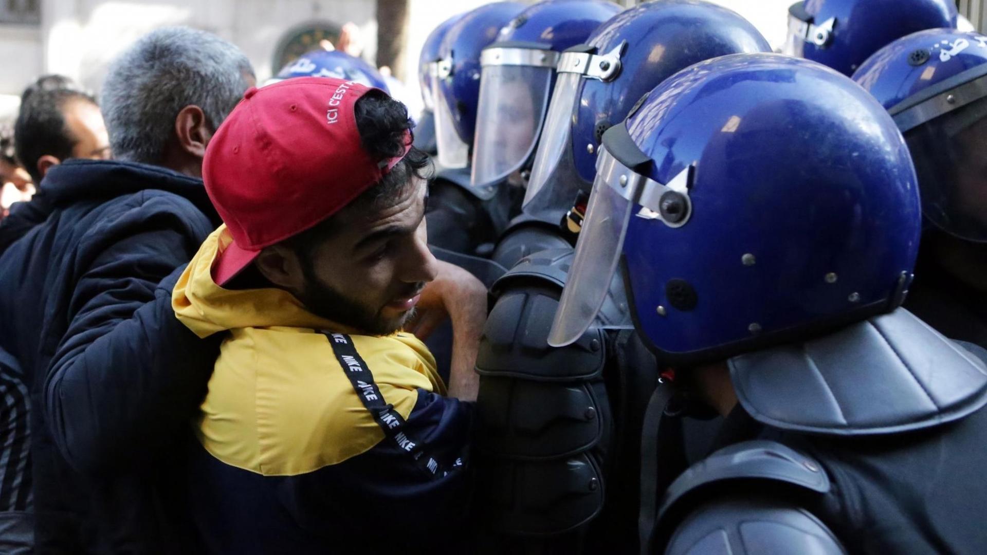 Protestierender steht in einer Demonstation einem blau uniformierten Polizisten gegenüber Protestierender steht in einer Demonstation einem blau uniformierten Polizisten gegenüber