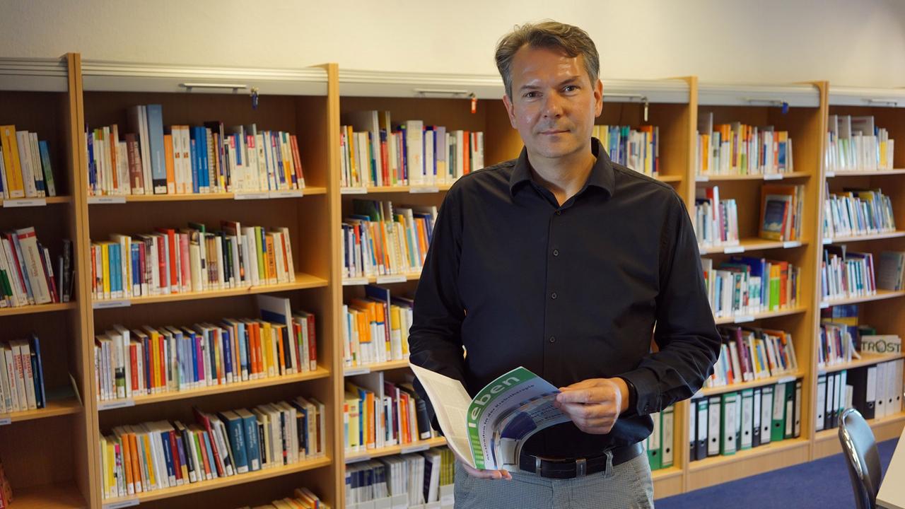 Frank Weise, Geschäftsführer der Krebsgesellschaft Sachsen-Anhalt, steht mit einem Buch in der Hand vor einem Bücherregal. Frank Weise, Geschäftsführer der Krebsgesellschaft Sachsen-Anhalt, steht mit einem Buch in der Hand vor einem Bücherregal.
