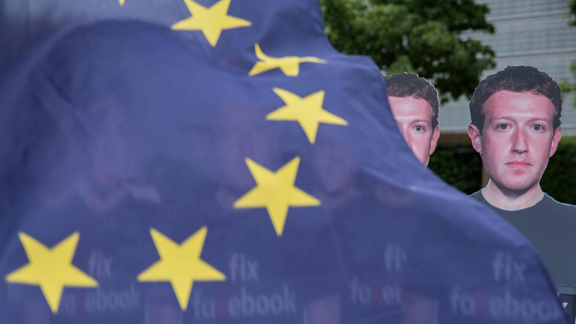 Eine EU-Flagge weht vor mehreren Pappaufstellern von Facebook-Chef Mark Zuckerberg