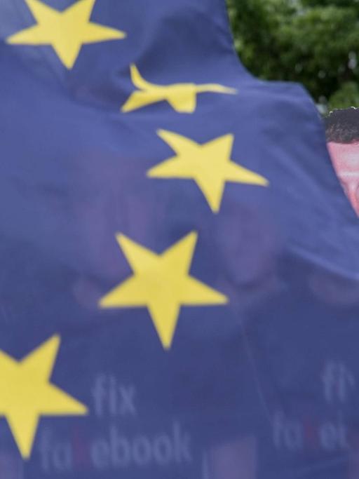 Eine EU-Flagge weht vor mehreren Pappaufstellern von Facebook-Chef Mark Zuckerberg
