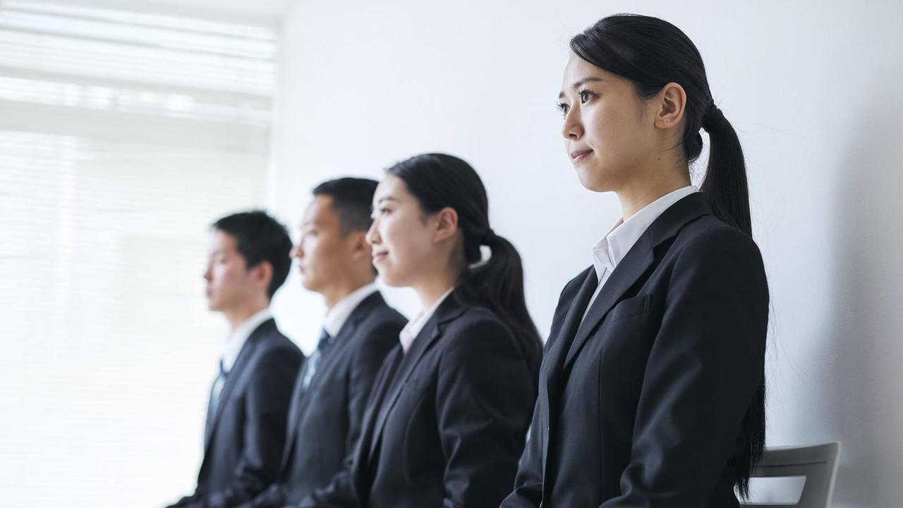 Zwei junge japanische Frauen und zwei junge japanische Männer tragen den typischen "Recruit Suite", den angehende Arbeitnehmer tragen müssen. Zwei junge japanische Frauen und zwei junge japanische Männer tragen den typischen "Recruit Suite", den angehende Arbeitnehmer tragen müssen.
