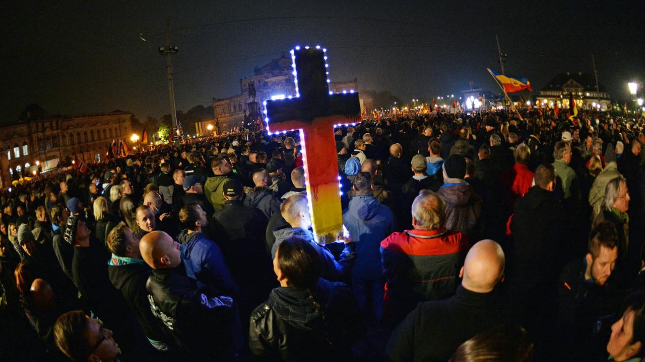 Tausende Anhänger des Bündnisses Pegida stehen auf dem Theaterplatz in Dresden, in der Mitte ist ein in Schwarz-Rot-Gold angemaltes Kreuz zu sehen. aufgenommen am 19.10.2015 Tausende Anhänger des Bündnisses Pegida stehen auf dem Theaterplatz in Dresden, in der Mitte ist ein in Schwarz-Rot-Gold angemaltes Kreuz zu sehen. aufgenommen am 19.10.2015