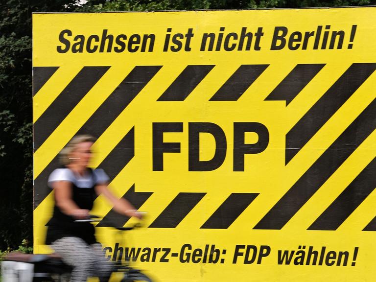 Eine Frau fährt auf dem Fahrrad am 28.07.2014 an einem Wahlplakt der FDP zur kommenden Landtagswahl mit dem Spruch "Sachsen ist nicht Berlin!" in Leipzig (Sachsen) vorbei. Die FDP regiert derzeit noch im sächsischen Landtag gemeinsam mit der CDU.