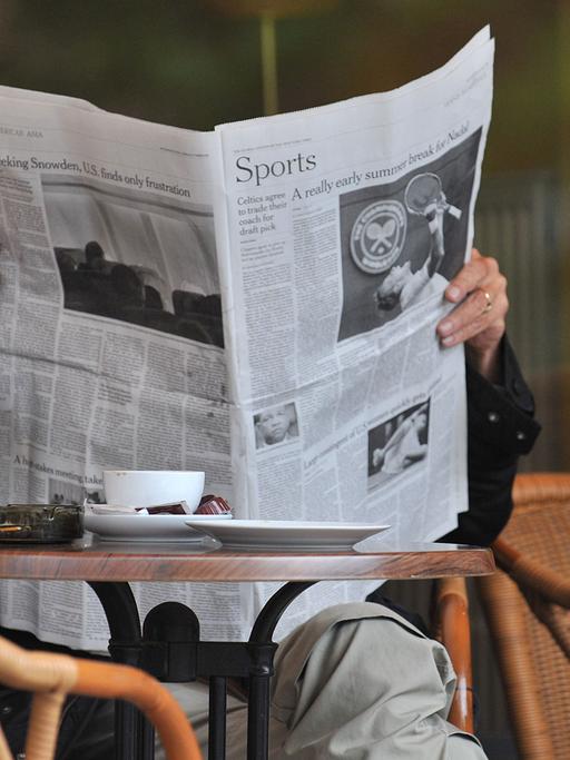 Ein Mann sitzt in einem Cafe und liest eine Zeitung.