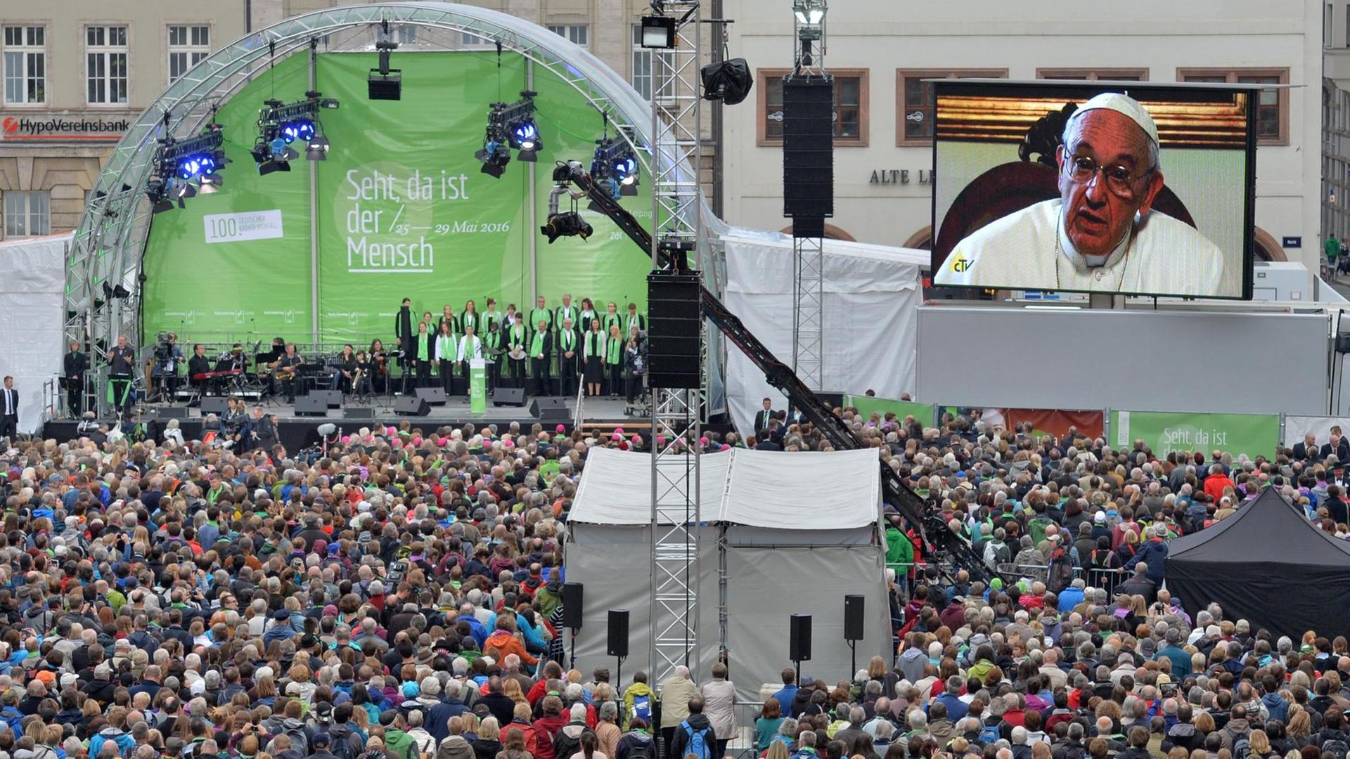 Papst Franziskus spricht am 25.05.2016 in einer Videobotschaft zur Eröffnung des Katholikentags in Leipzig zu einer Menschenmenge, die vor einer Bühne steht. Papst Franziskus spricht am 25.05.2016 in einer Videobotschaft zur Eröffnung des Katholikentags in Leipzig zu einer Menschenmenge, die vor einer Bühne steht.